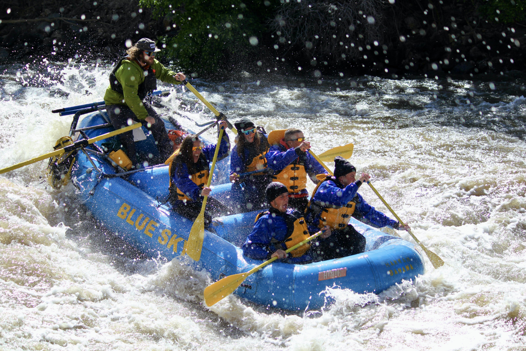 A photo of a raft going through rapids on a Half Day Rafting Adventure. The boat is full of people and they all look excited.