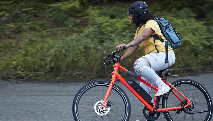 In this image, a girl flashes a bright smile as she zips along on a vibrant red Mission e-bike.