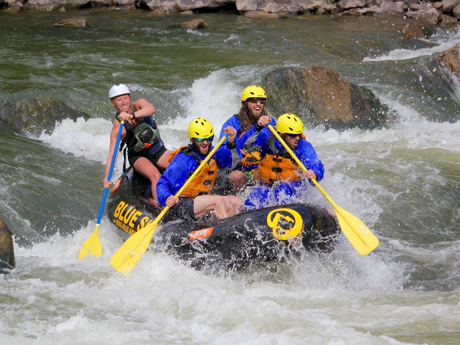 In this exhilarating image, three individuals, accompanied by their guide, expertly navigate a Mini Max through Class III waters. Adorned in vibrant safety gear, they joyously experience the thrill of the rapids, their smiles radiating the sheer excitement of the adventure.